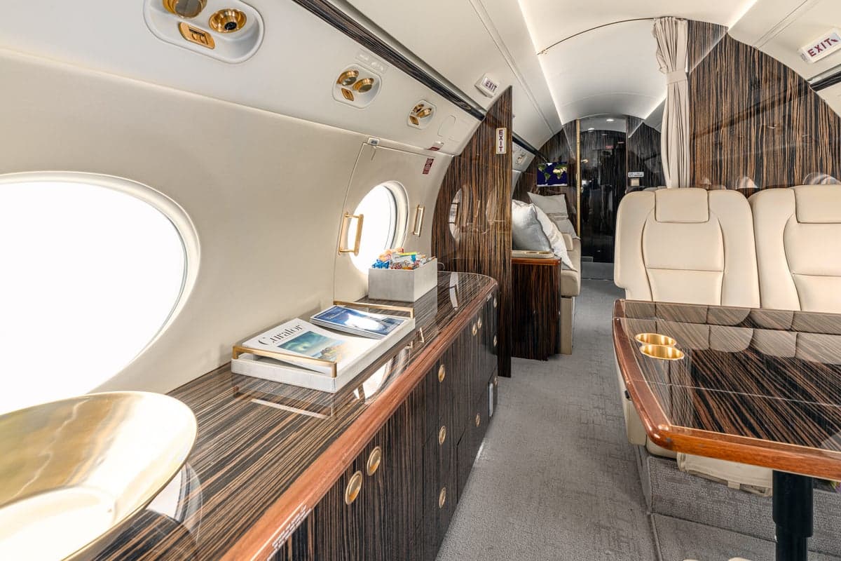 The interior of the aircraft features a table with cup holders and cream-colored leather seats.