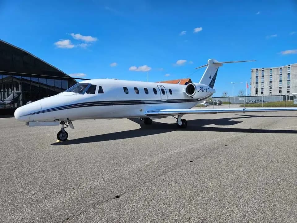 A white business jet with black and blue stripes on the tarmac under a blue sky.