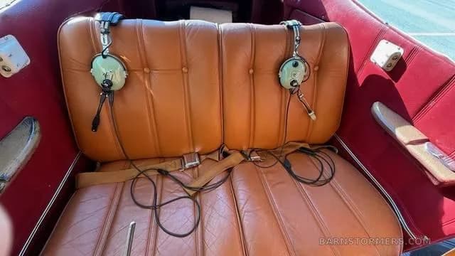 The rear brown leather seats of a small aircraft cabin, with two aviation headsets resting on them.
