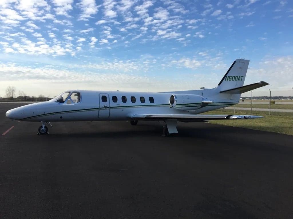 Side profile of a white Cessna CitationJet with green stripes.