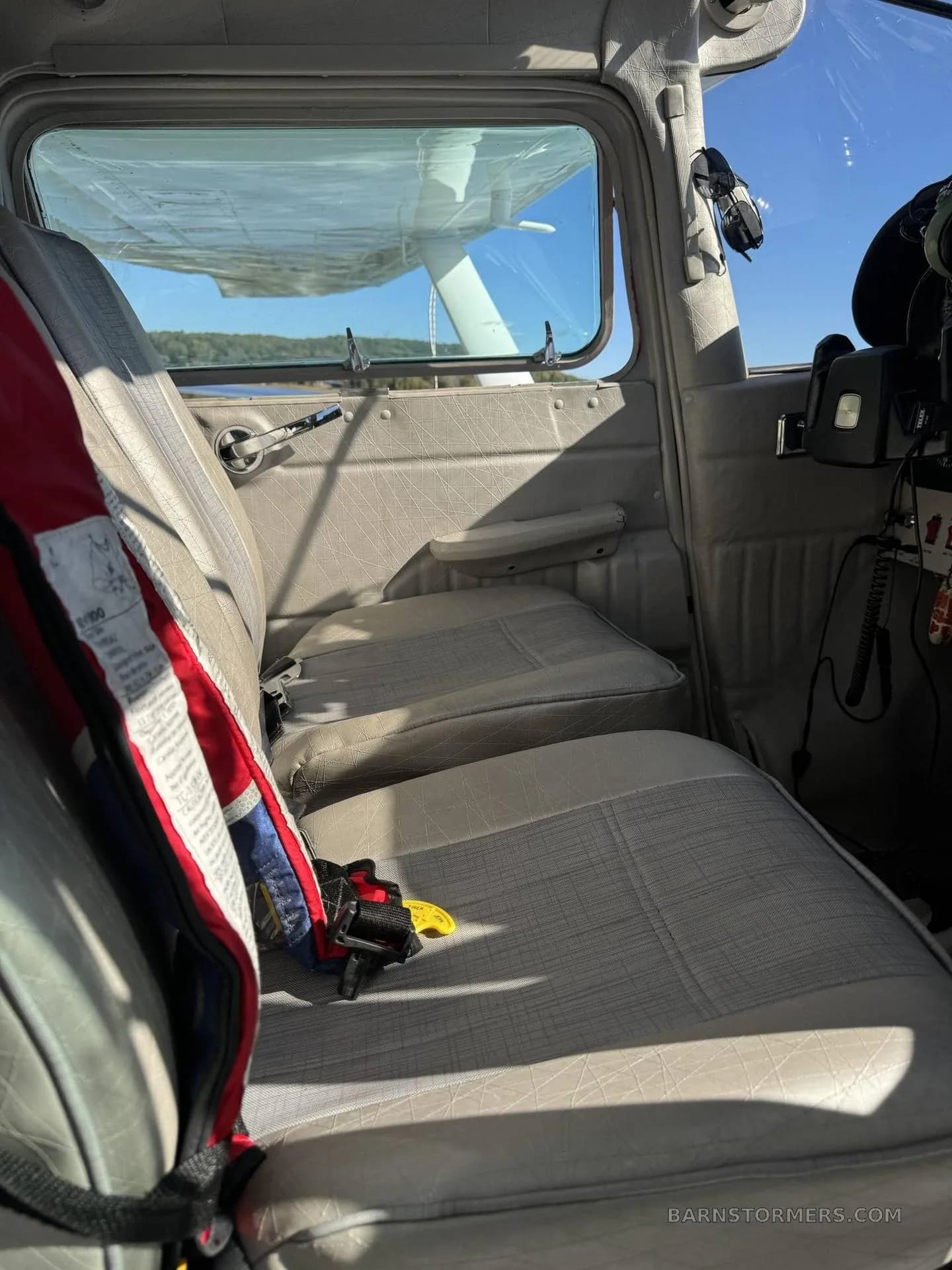 The light gray interior cabin seats of the aircraft, with a red life vest on the front seat.