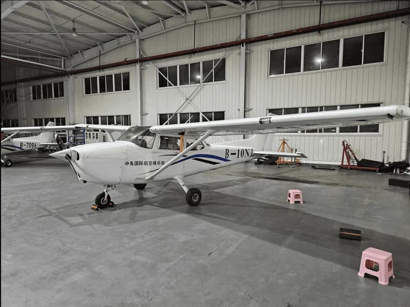 A white single-engine aircraft with blue and black stripes and registration B-10NJ parked in a hangar.