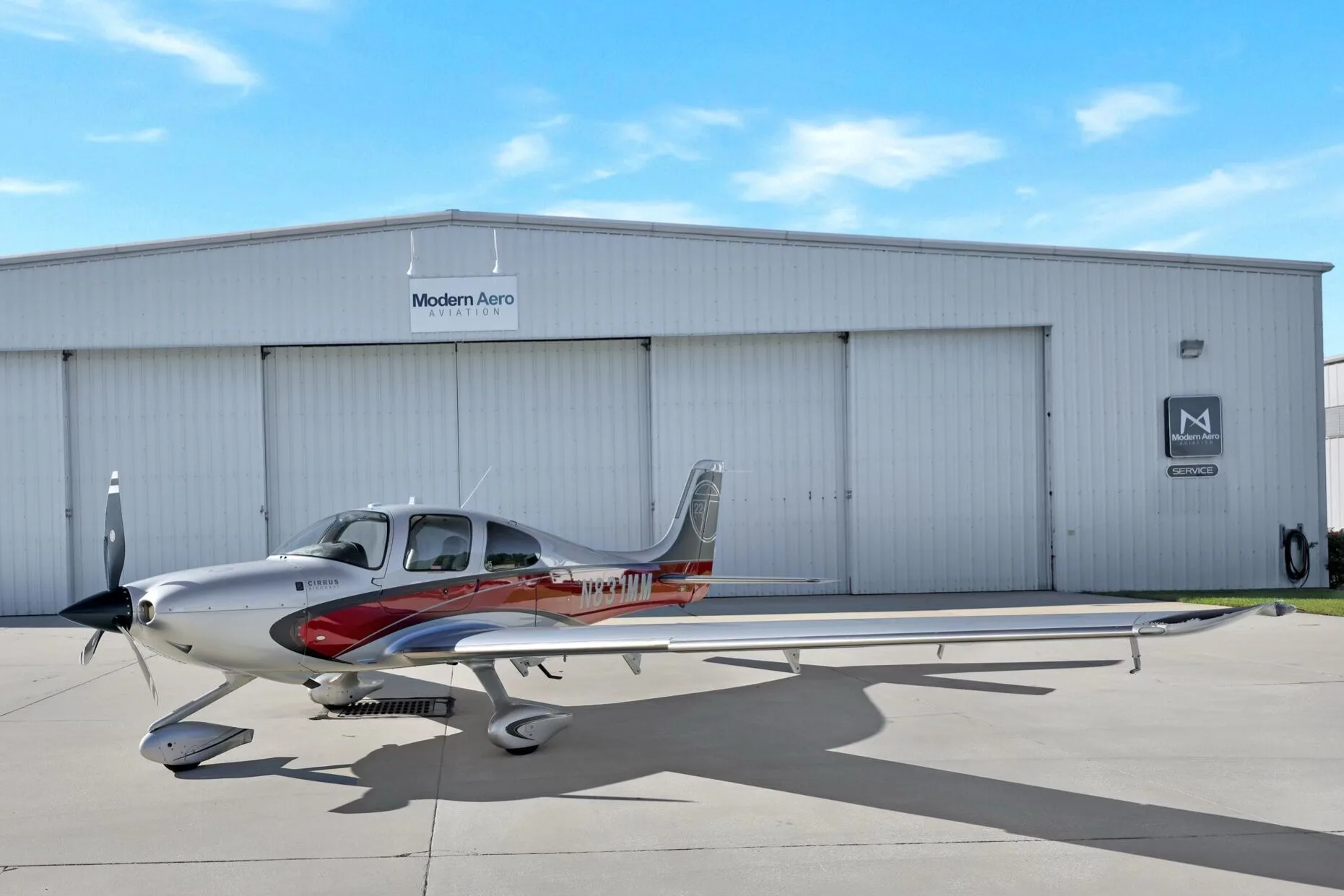 Side view of a Cirrus SR22T aircraft with red and silver paint scheme, registration N831MM, parked on an airfield with doors closed.