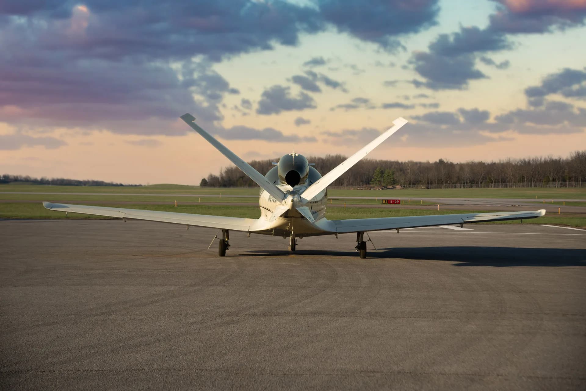 A rear view of a white Cirrus Vision Jet parked on an airfield under a cloudy sky.