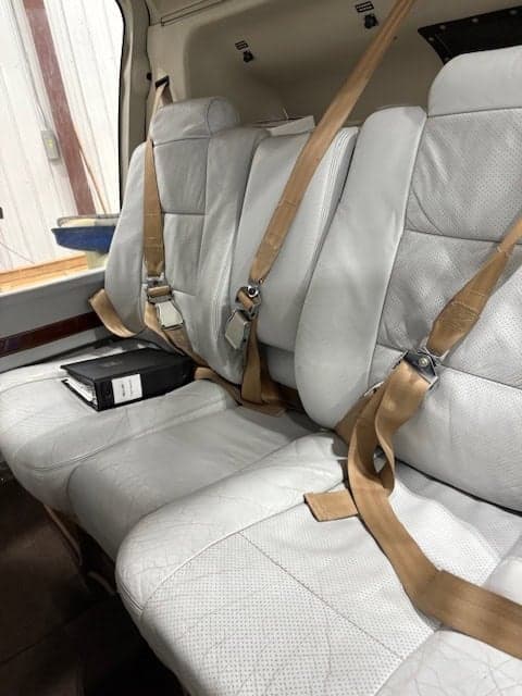 The interior of the helicopter is shown with white leather seats and tan seatbelts.
