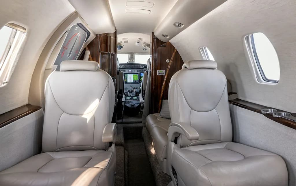 The aircraft cabin interior with light leather seats, looking forward towards the open cockpit door.