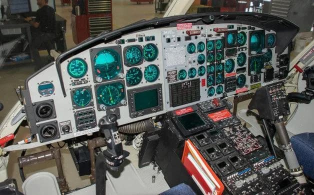 The cockpit of a helicopter features numerous green-lit gauges, screens, and control panels.
