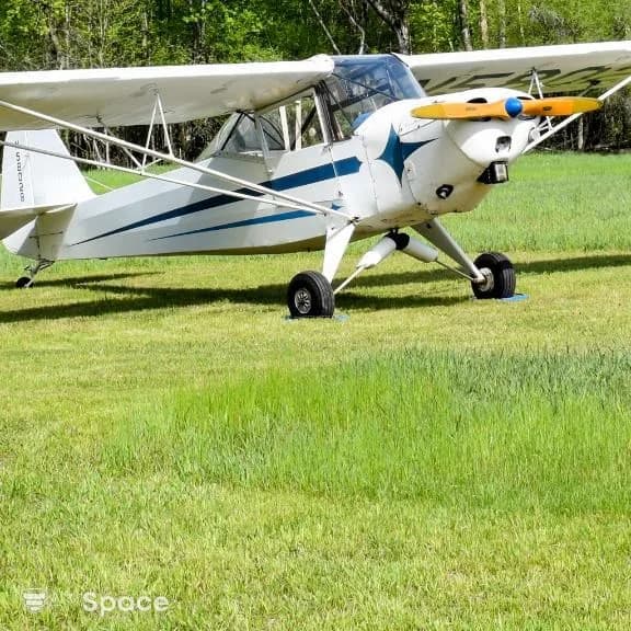 A white Cessna Skylane with black and blue accents is parked inside a hangar with an American flag and Kansas flag hanging in the background.