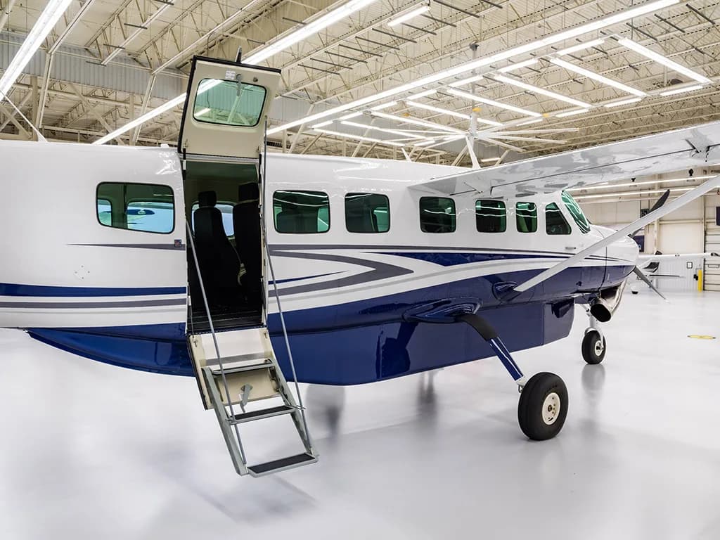 A close-up view of the white and blue Cessna Caravan with its passenger door and integrated stairs open in a hangar.