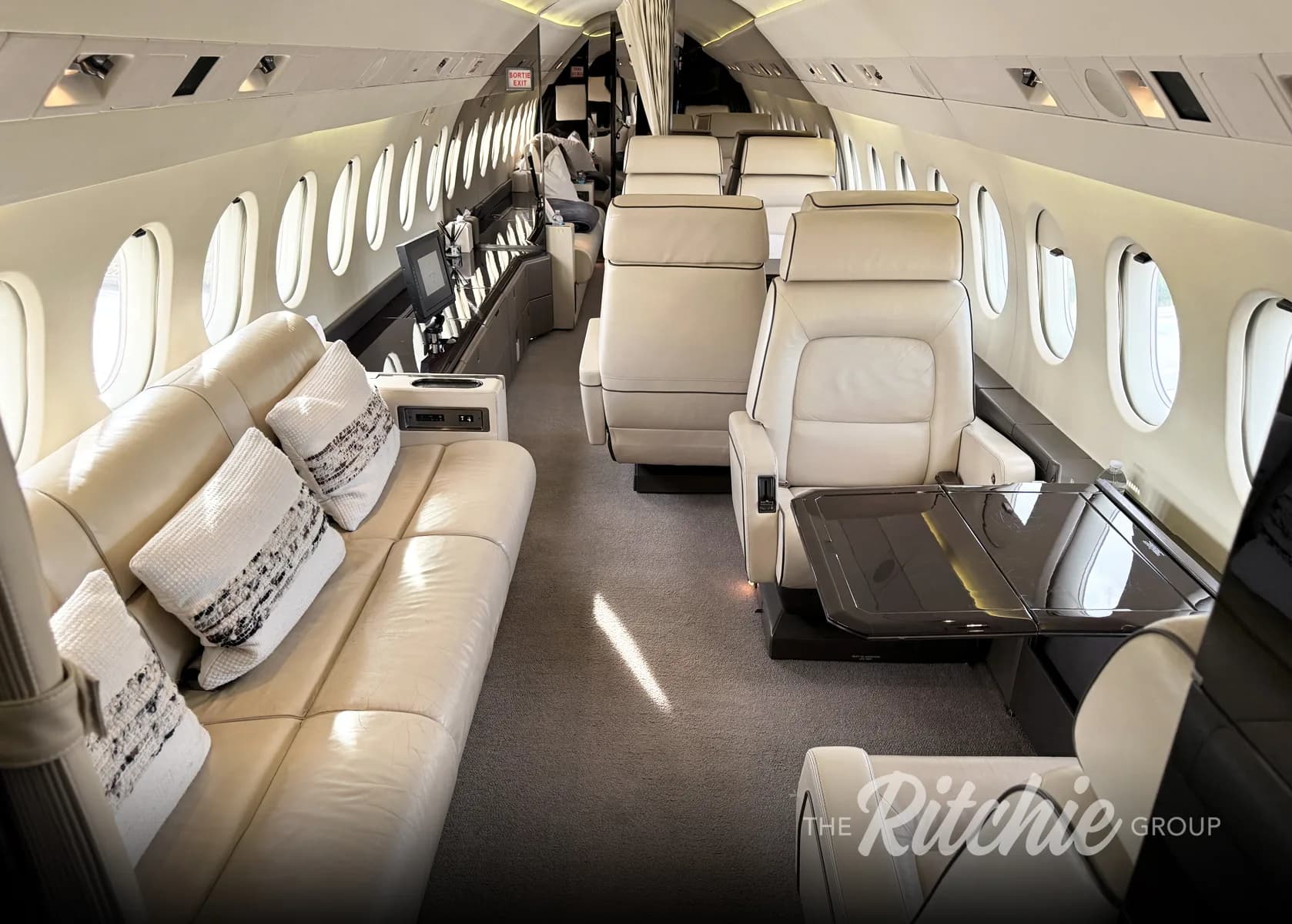 The luxurious interior cabin of a private jet, featuring cream leather seating, a sofa, and individual chairs with tables.