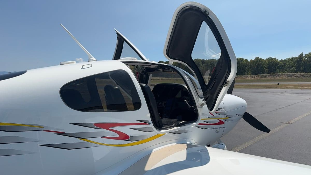 Side view of a Cirrus aircraft with its doors open, showing the cockpit and interior.