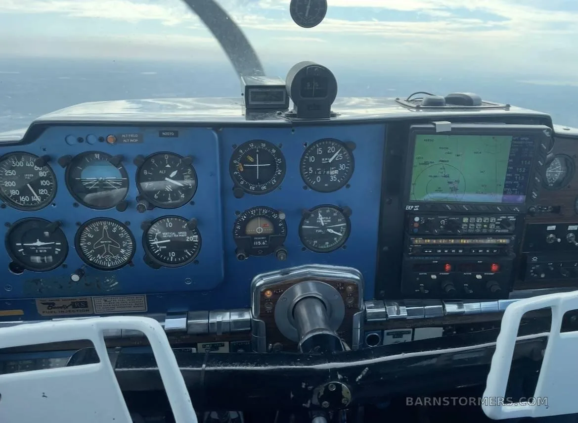 The blue instrument panel of a small aircraft with various gauges, a GPS display, and a control yoke, seen from the pilot's perspective during flight.