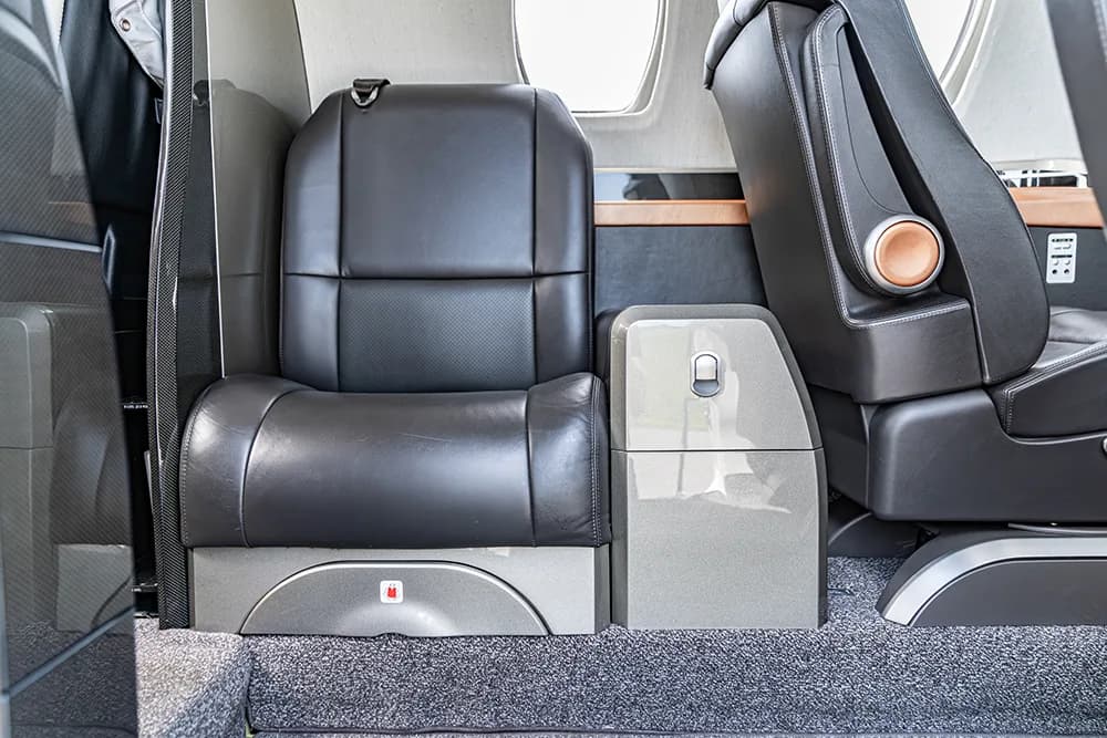 A close-up of the aircraft cabin interior showing a single dark leather seat and a small storage unit.