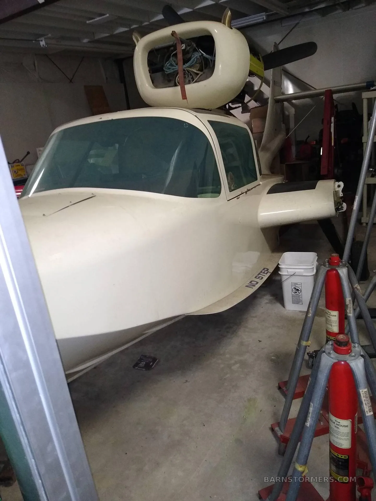 The front of a white aircraft, with its engine nacelle visible above the cockpit, is parked inside a workshop.