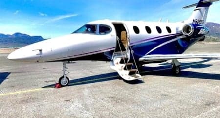 A white and blue jet with an open door sits on the tarmac.