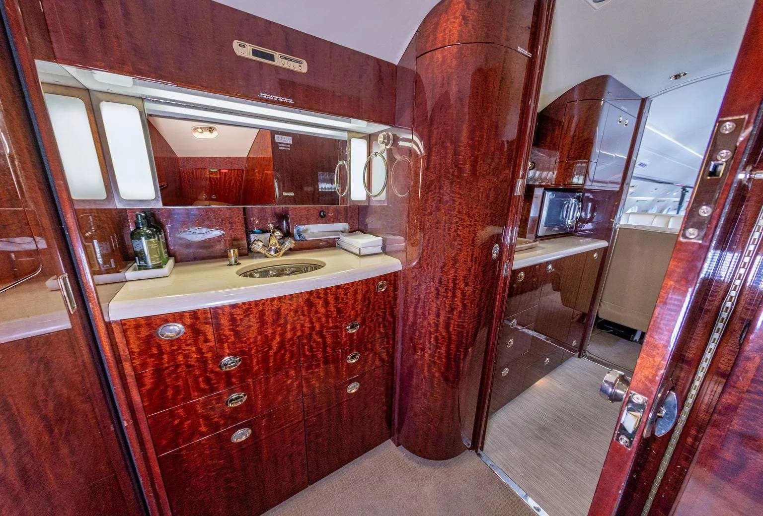 The aircraft lavatory with a sink, mirror, and polished wood cabinetry.