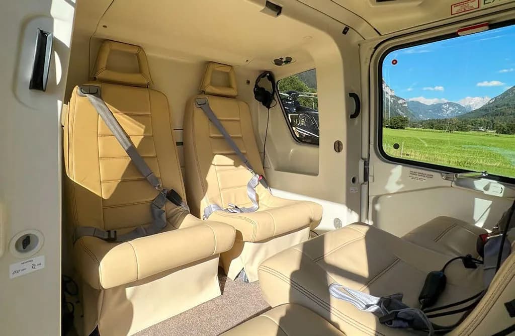 A wider view of the helicopter's beige interior cabin with multiple seats and a scenic mountain view outside.
