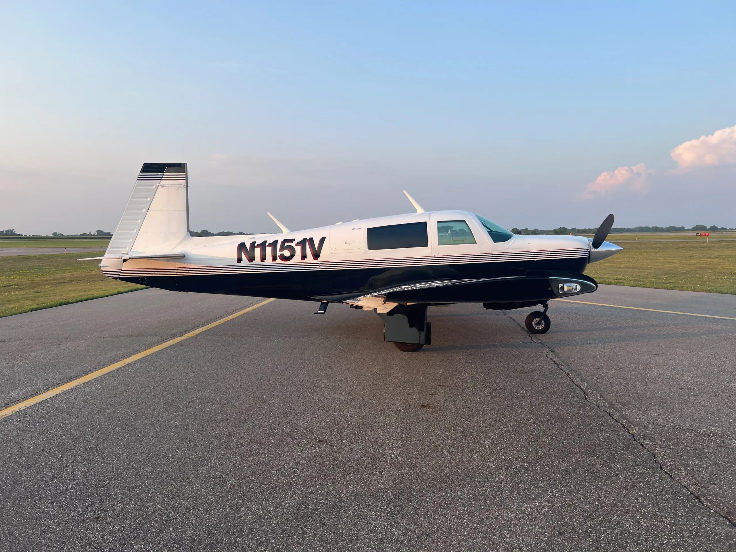 A white and dark blue single-engine aircraft, N1151V, parked on an asphalt runway at sunset.
