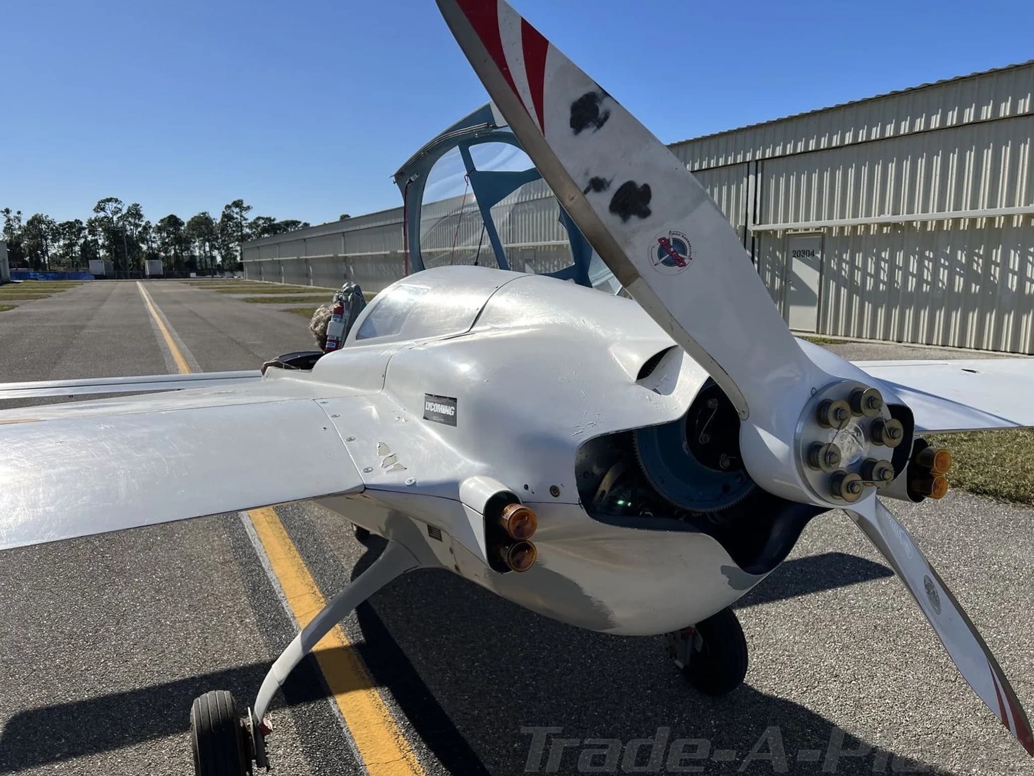 A close-up front view of a white experimental aircraft showing its large propeller and exposed engine components.