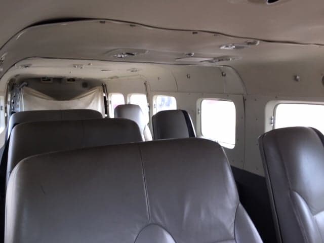 The interior cabin of a Cessna Caravan aircraft, showing multiple rows of grey passenger seats.