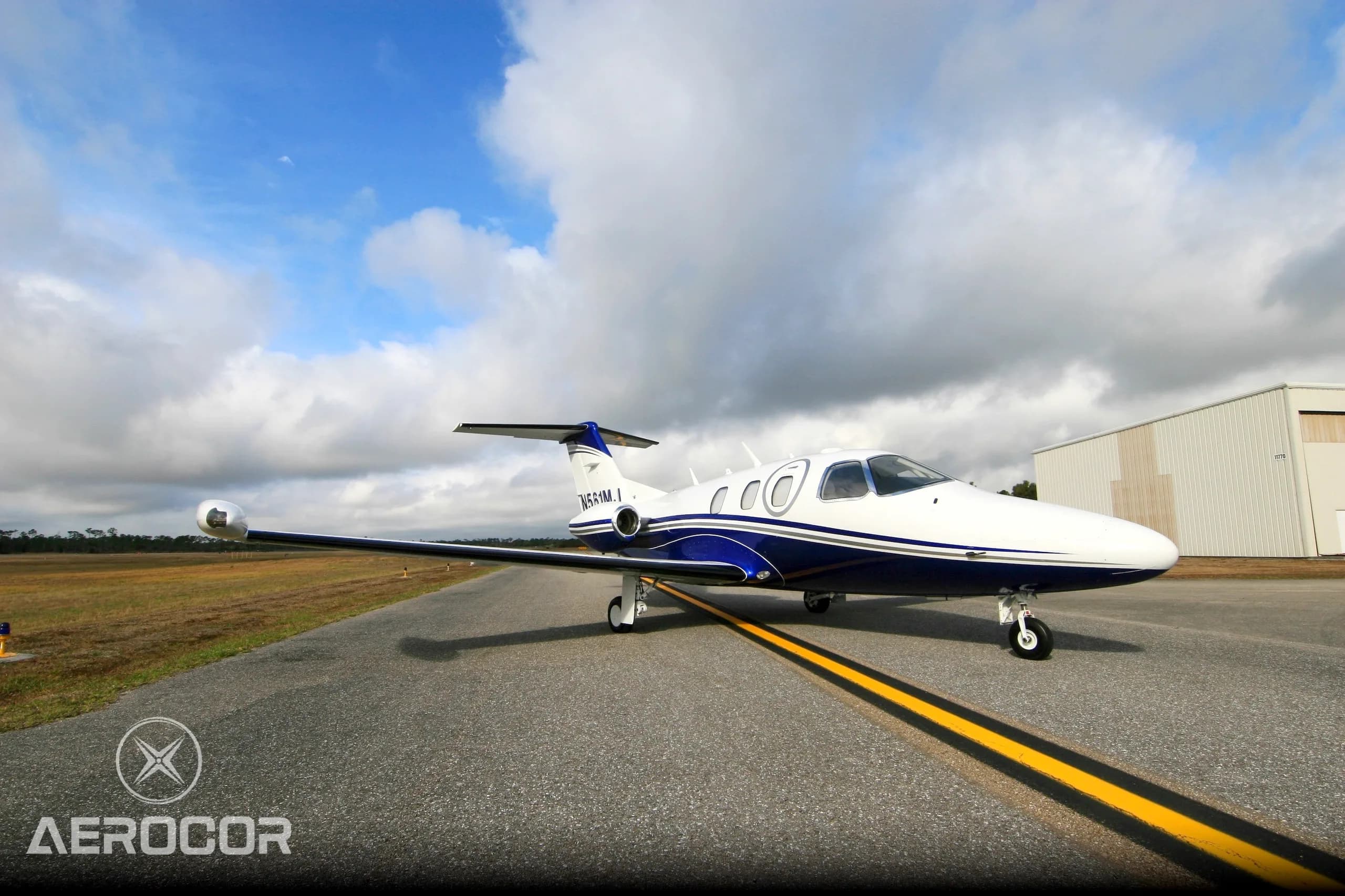 A white and blue Eclipse 500 jet, registration N561MJ, parked on an airfield under a partly cloudy sky.