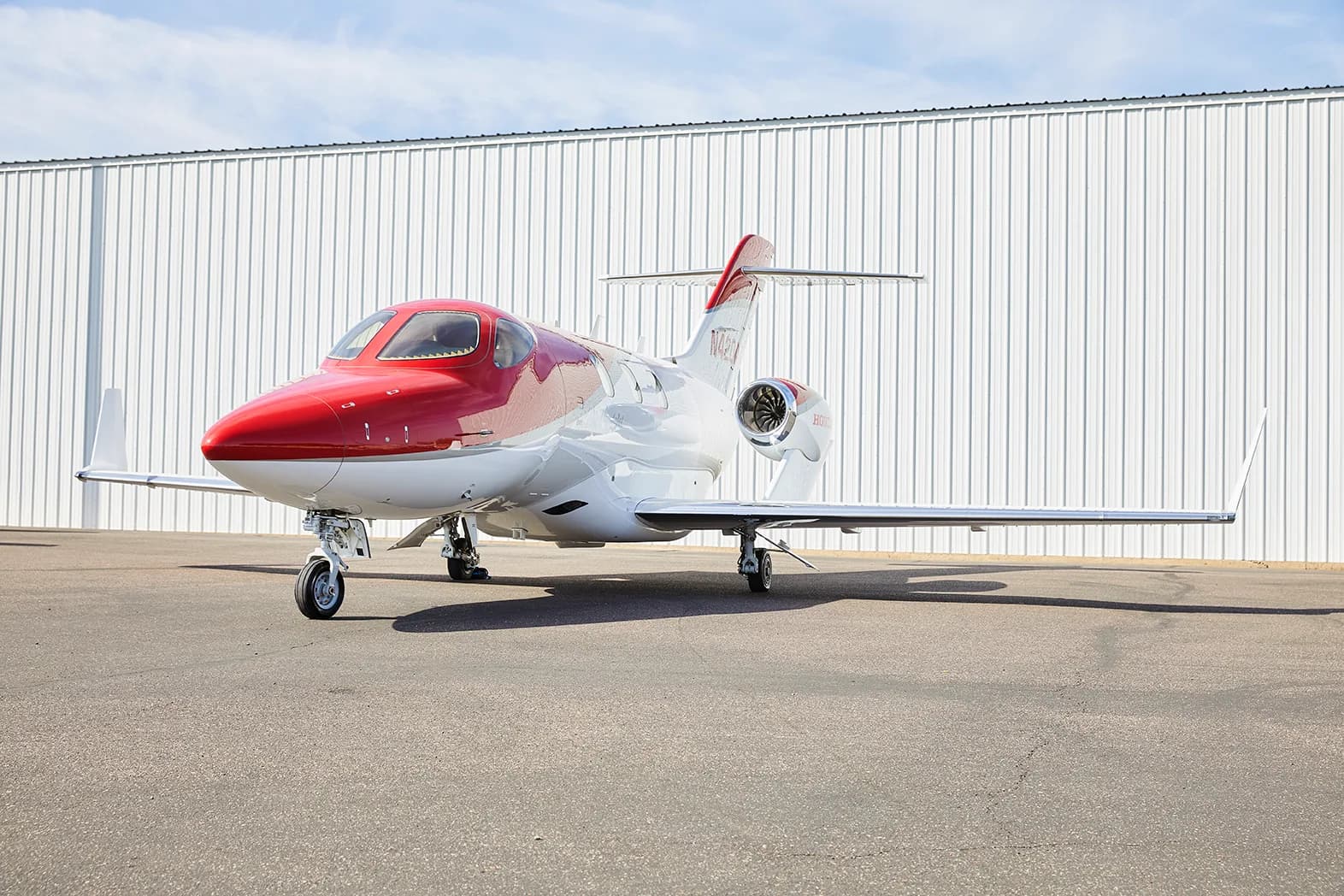 A red and white HondaJet HA-420 aircraft, registration N420AZ, is parked on an asphalt tarmac in front of a white hangar.
