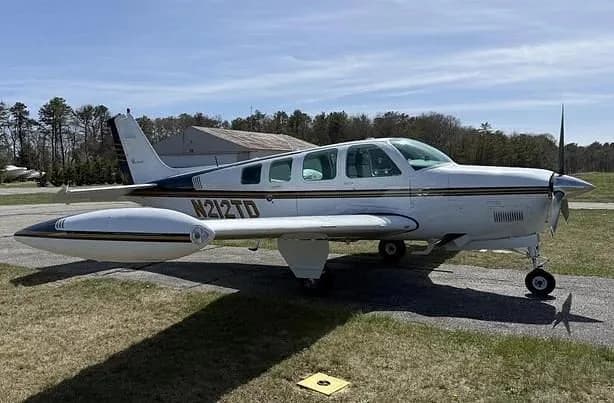 A white Beechcraft Baron N212TD with dark and gold stripes is parked on an airfield ramp.