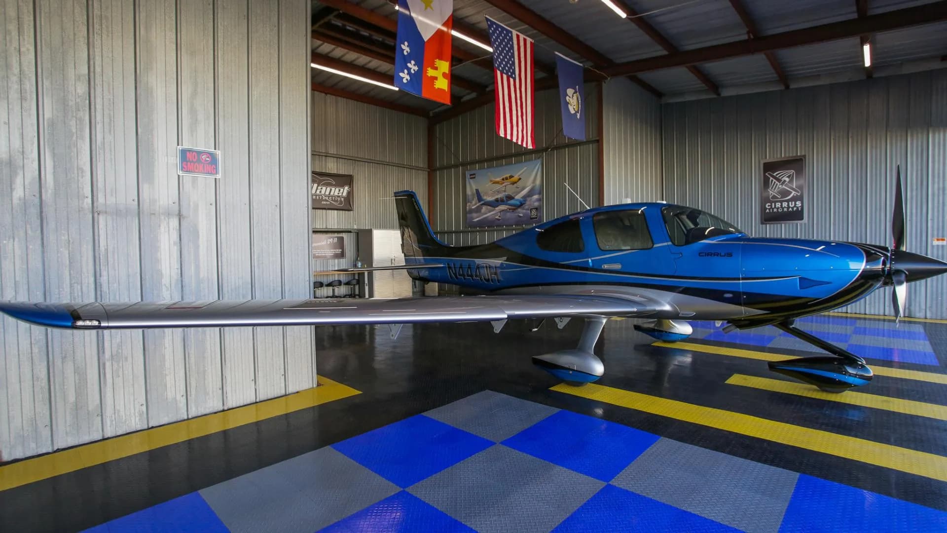 A blue and silver Cirrus SR22 aircraft with registration N444JH parked inside a hangar.