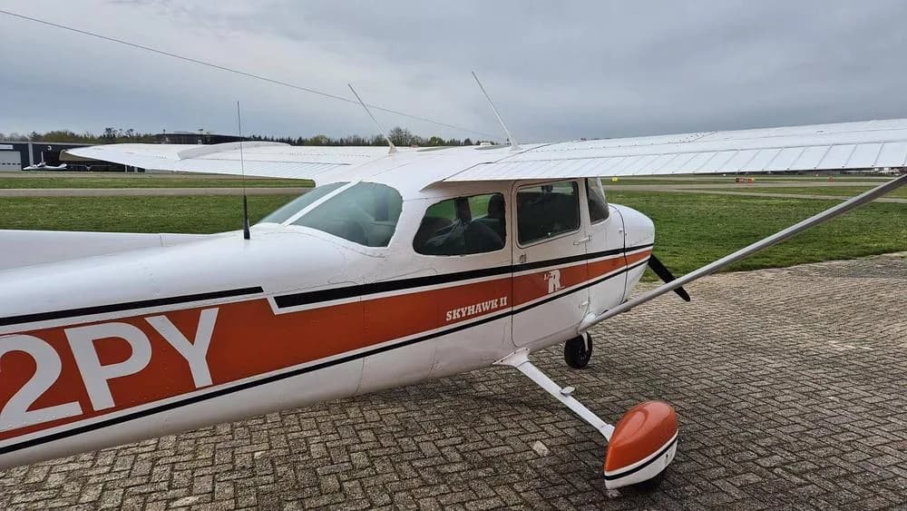 A close-up view of the front fuselage and wing of the white and orange Cessna Skyhawk II N202PY.