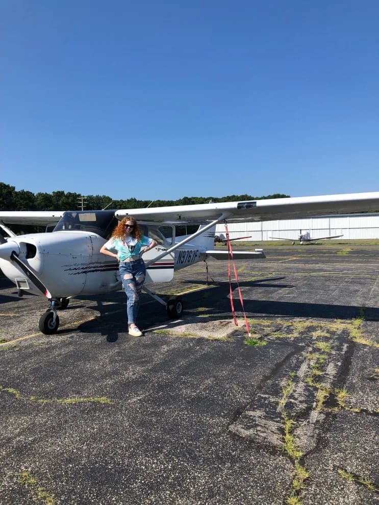 Woman standing in front of a Cessna 172 Skyhawk aircraft on the tarmac.