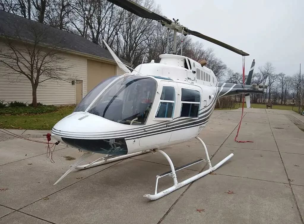 A white helicopter with dark grey stripes parked on a concrete driveway.