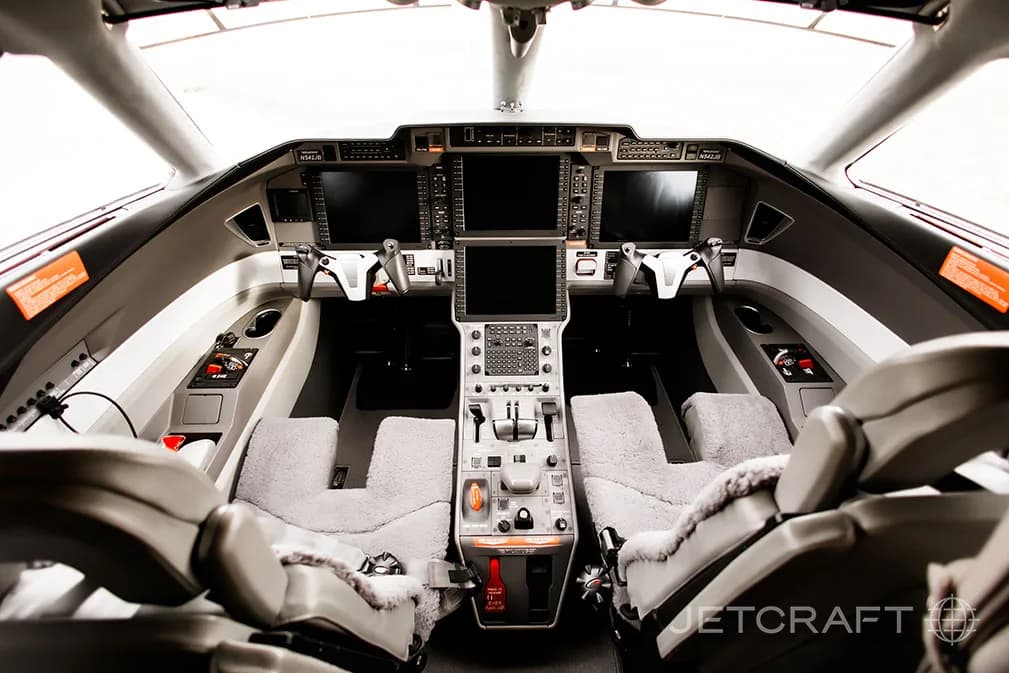 The modern cockpit of a private jet, featuring multiple digital displays, control yokes, and a central throttle quadrant.