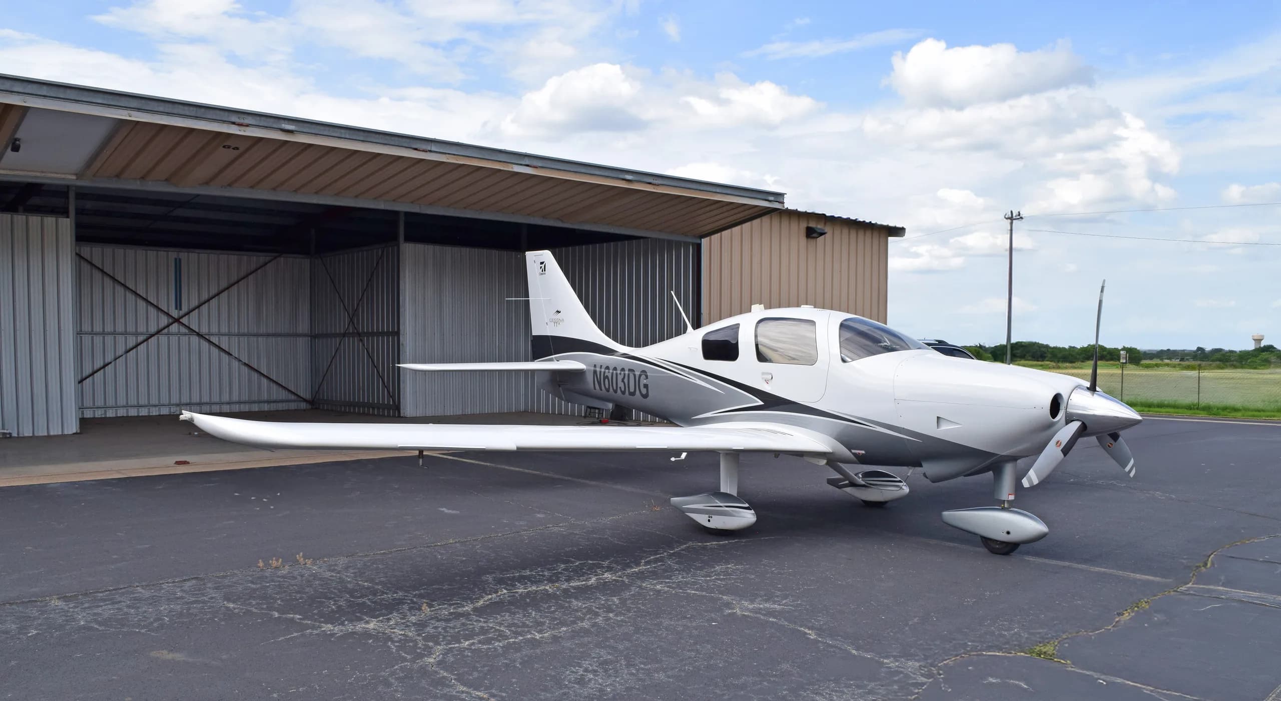 A white and grey Cessna TTx aircraft, N603DG, parked on an asphalt apron with a hangar in the background.