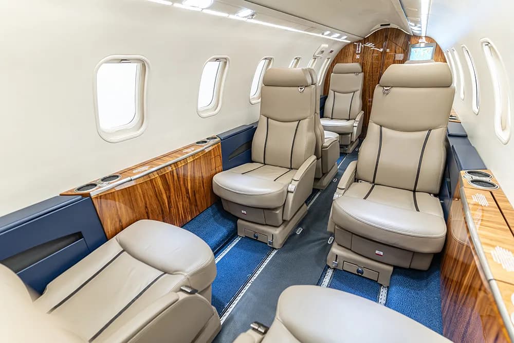 A view of the aircraft cabin interior from the front, showing tan leather seats and wood paneling.