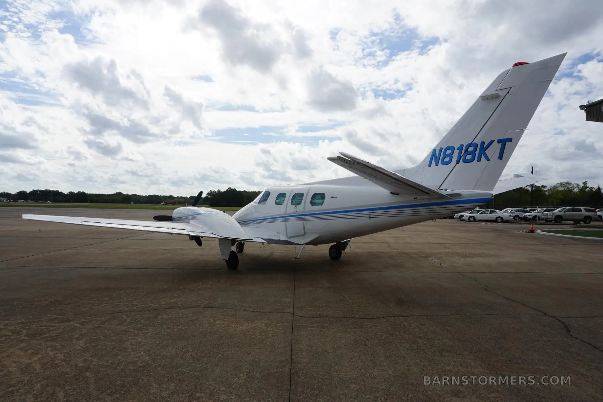 The rear-side view of a white twin-engine propeller aircraft with blue stripes (N818KT) parked on the tarmac.