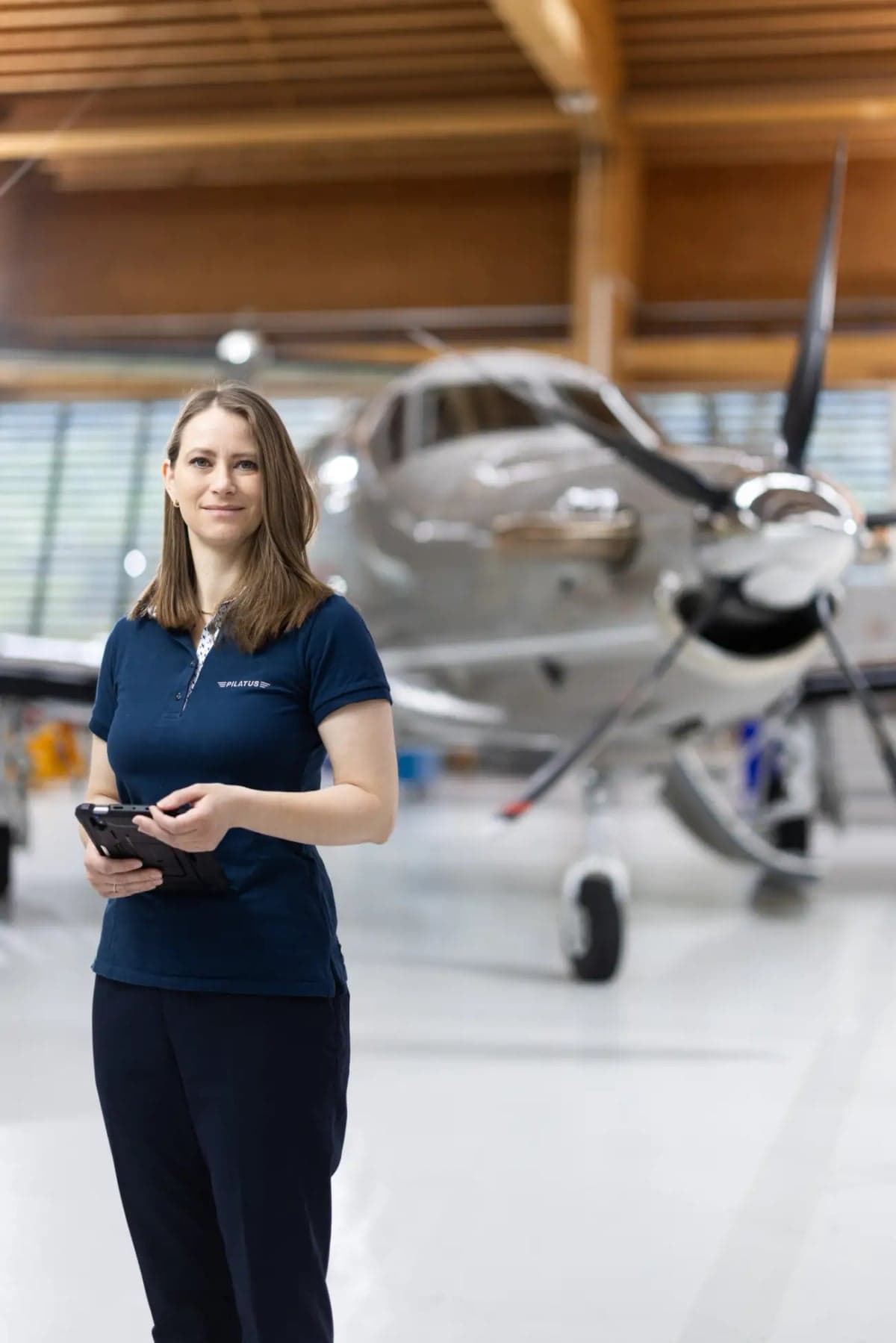 A woman stands in front of a Pilatus PC-12 aircraft in a hangar.