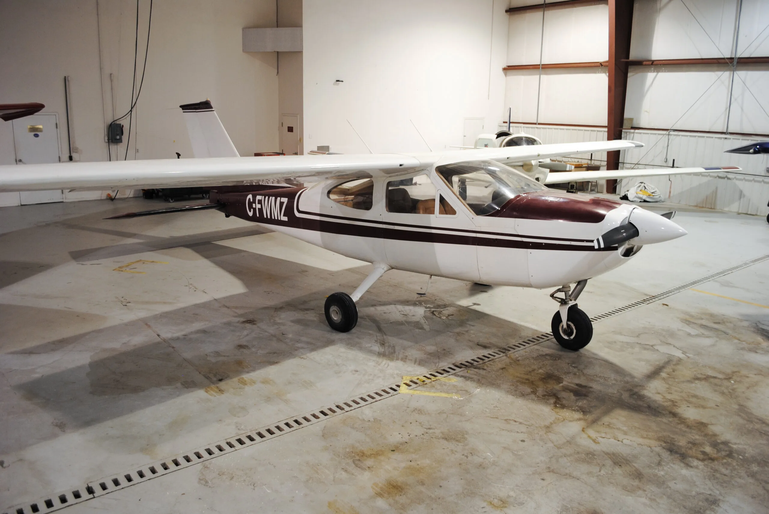 A Cessna 177 Cardinal aircraft with a maroon and white paint scheme parked in a hangar.