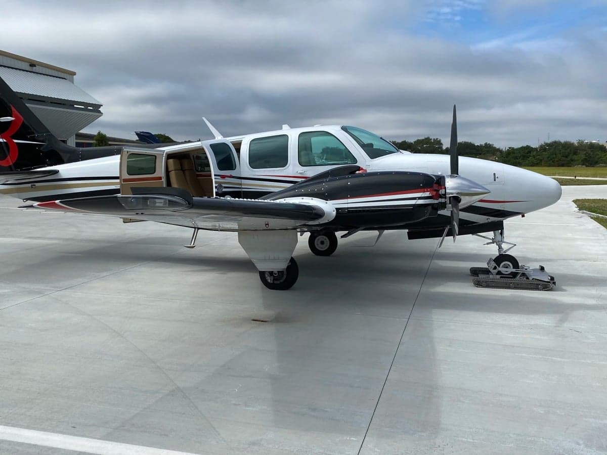 A white and black twin-engine aircraft with registration N581PS, parked on an airfield with its passenger door open.