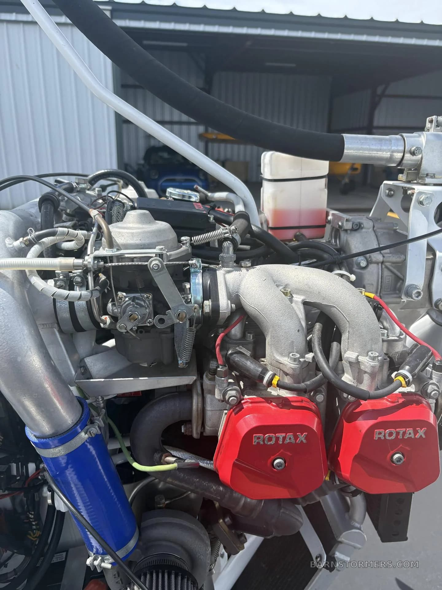 A close-up view of the exposed Rotax engine of the M-22 gyrocopter, showing carburetors and red valve covers.