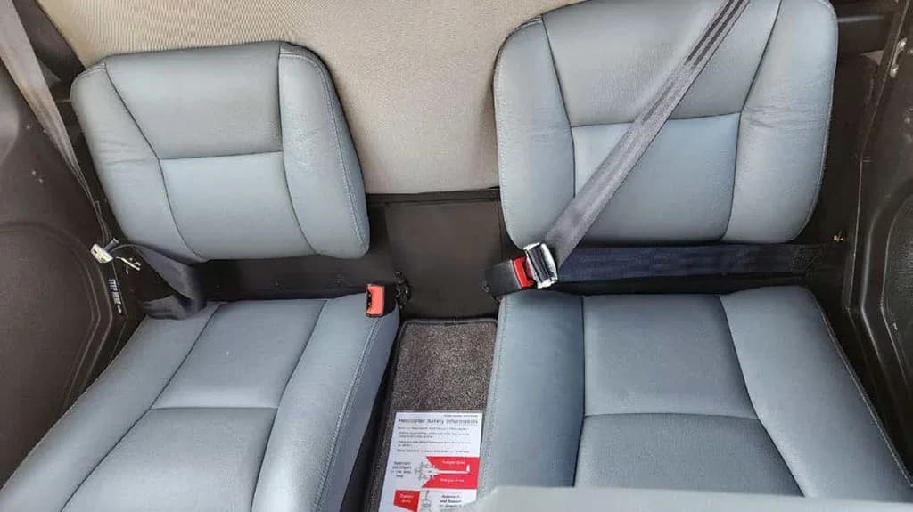 The gray leather rear seats of a helicopter cabin are visible, with seatbelts buckled.