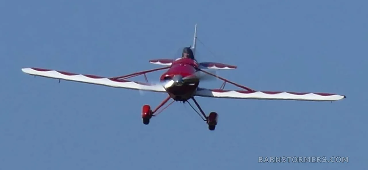 A red and white Spezio Tuholer monoplane, registration N99ER, flying directly towards the viewer against a clear blue sky.