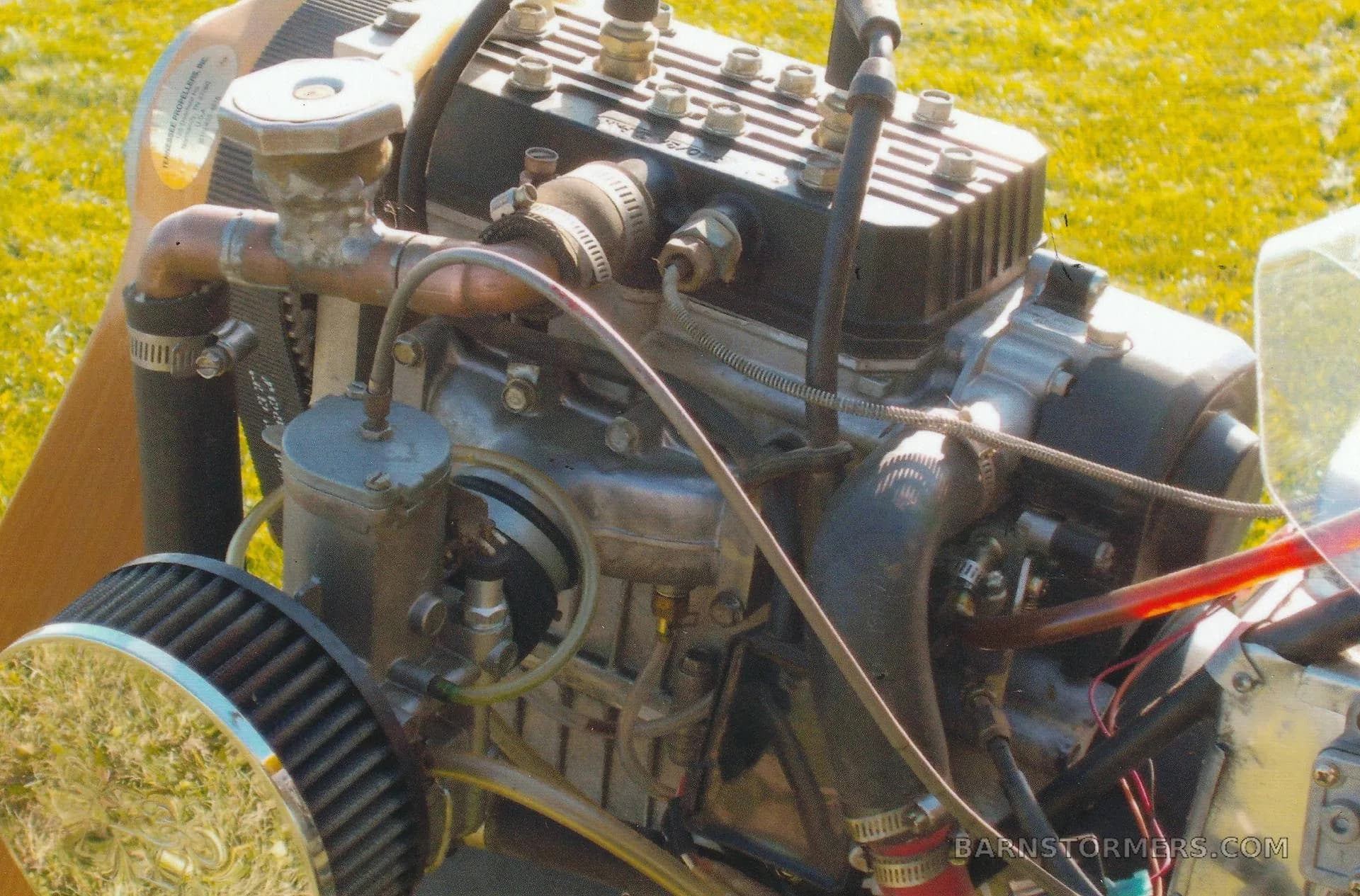 A detailed close-up of the exposed engine of an ultralight aircraft, showing its components and plumbing.