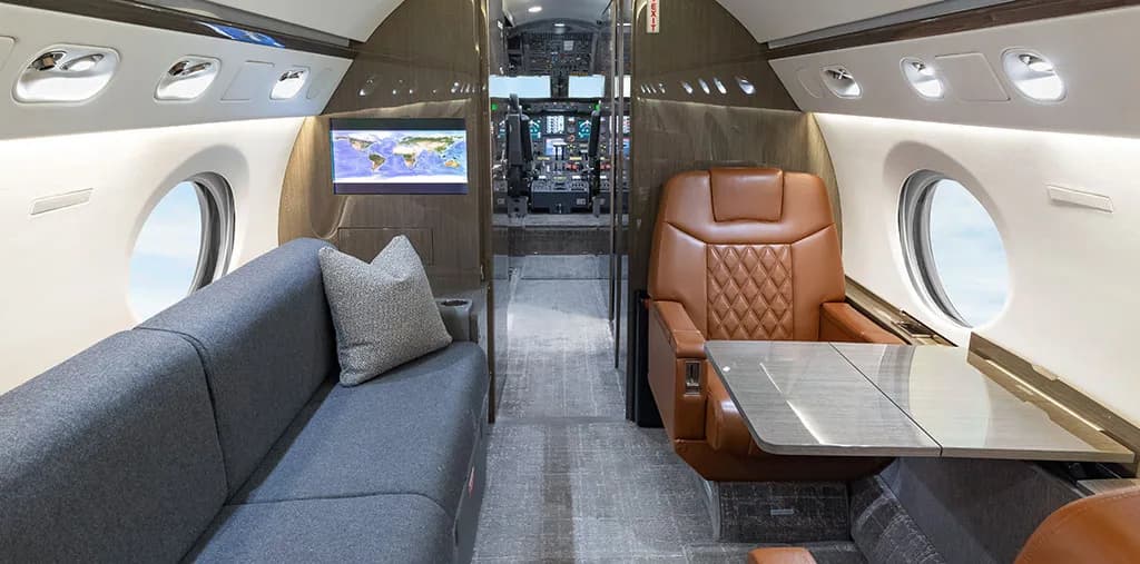 The aircraft cabin interior featuring a grey sofa, a brown leather seat, and a screen displaying a world map.