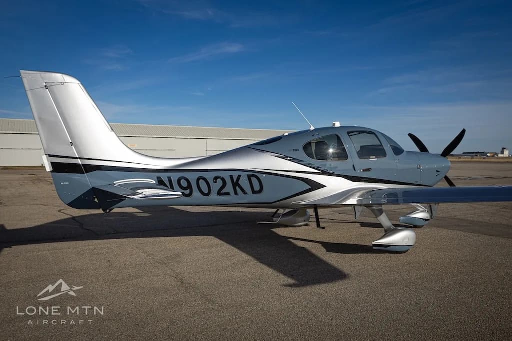 A side view of the Cirrus SR22T aircraft, N902KD, in blue and silver, parked on an airfield.