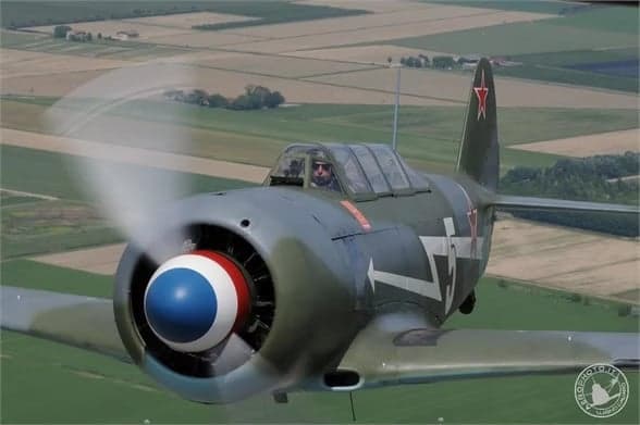 A close-up of a Lavochkin La-9 in flight with a gray and green paint scheme and a red star on the tail.