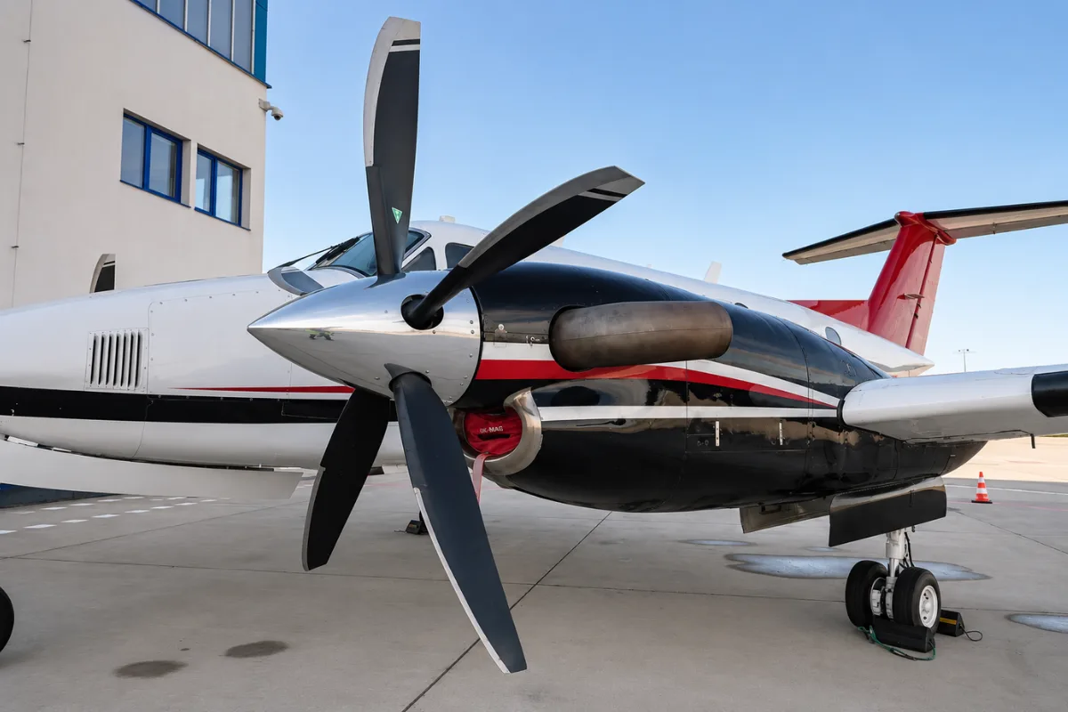A close-up view of the right engine and propeller of a white and red twin-engine turboprop aircraft.
