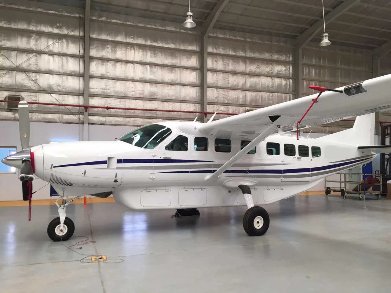 A white single-engine turboprop aircraft with blue and grey stripes is parked inside a hangar.