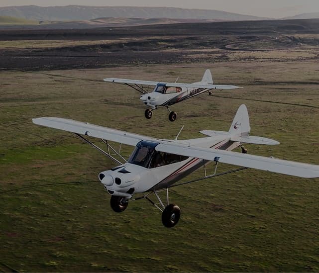 Two white and gray aircraft flying over a green field.