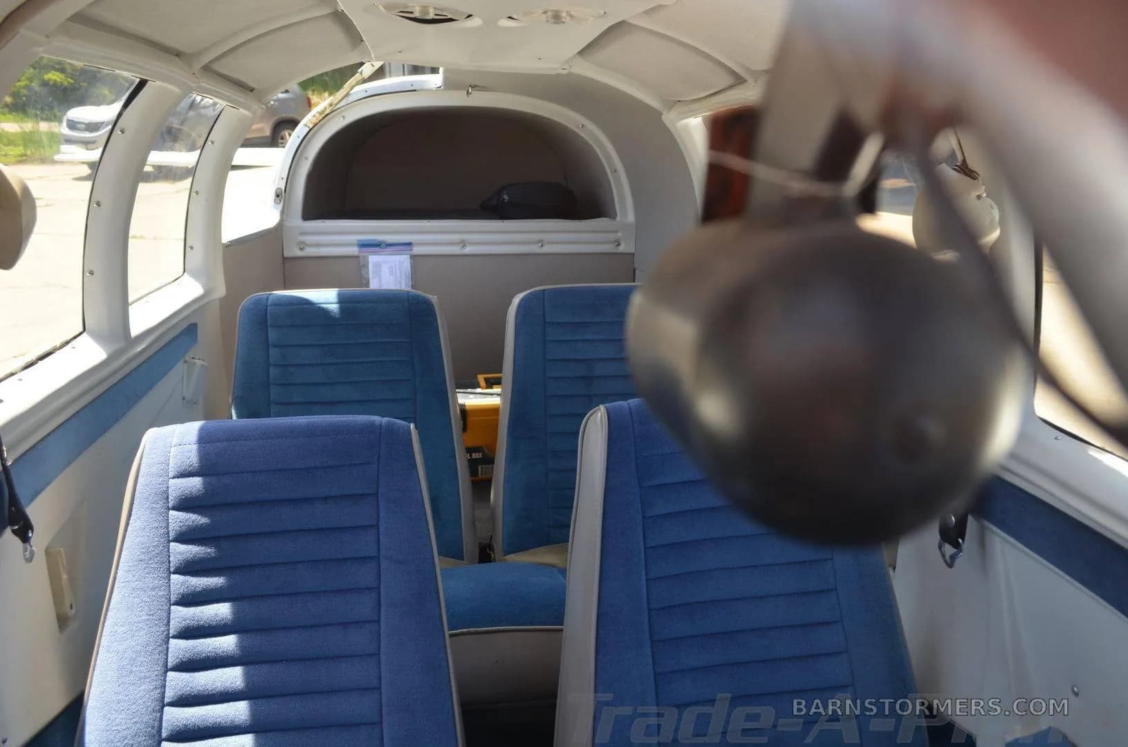 The interior cabin of a small aircraft shows four blue fabric seats and an aft baggage area.