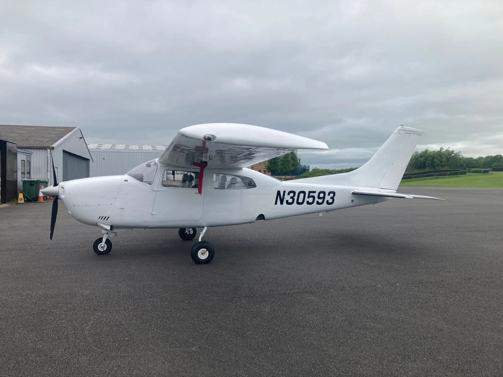 A white Cessna 172 aircraft with registration N30593 parked on an airfield tarmac next to a hangar.